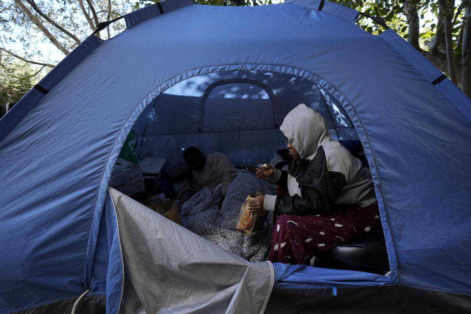 Grace Enjei, 24, right, and Daniel Ejuba, 20, migrants from Cameroon, sit in a blue tent behind the House of Cooperation located inside a United Nations-controlled buffer zone cutting across Nicosia, the capital of ethnically divided Cyprus on Wednesday, Dec. 1, 2021. The Cameroonian asylum seekers crossed from the island's breakaway Turkish Cypriot north about six months ago and got stuck in the buffer zone amid a Cypriot government crackdown on migrants crossing the porous buffer zone. (AP Photo/Petros Karadjias)