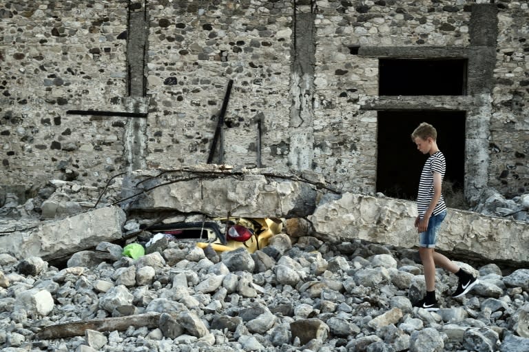 A boy stands next to a car crushed under rubble near the port of the Greek island of Kos following a 6.5 magnitude earthquake which struck the region on July 21, 2017