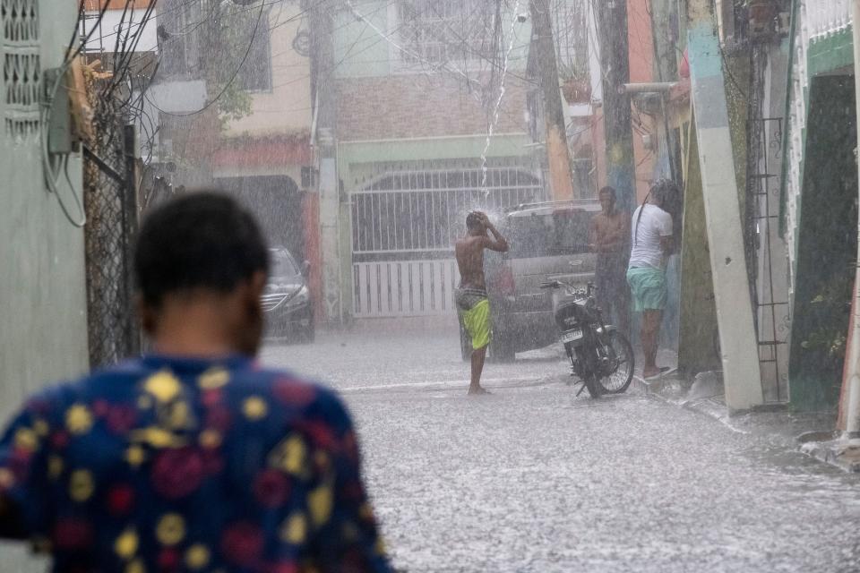 A man stands under a roof drain as rain from Tropical Storm Franklin falls on Santo Domingo, Dominican Republic, on Tuesday.