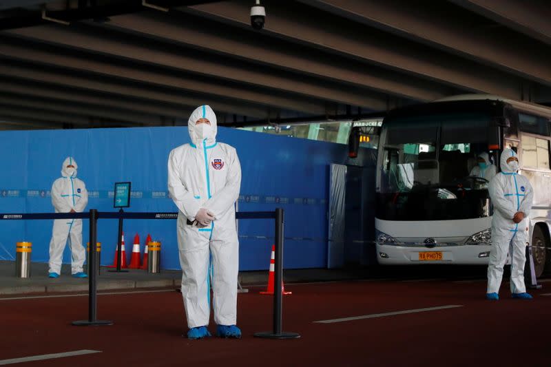 Staff members in protective suits stand guard next to a bus before the expected arrival of a World Health Organisation (WHO) team in Wuhan