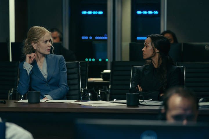 Two women look at each other while sitting in front of computers.