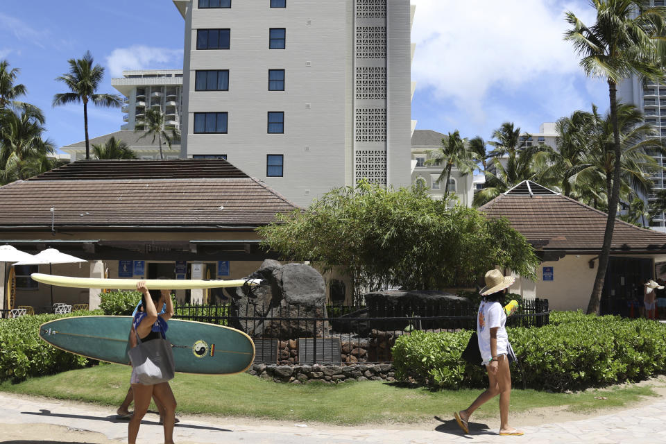 Beachgoers walk by the Kapaemahu stones at Waikiki beach in Honolulu on Tuesday, June 28, 2022. A new exhibit at Honolulu's Bishop Museum draws attention to the stones which honor four "mahu" healers from Tahiti who visited Hawaii more than five centuries ago. (AP Photo/Audrey McAvoy)