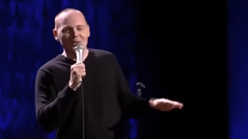 Bill Burr holding a microphone, making a joke in a stand up act.