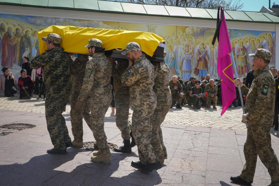 Ukrainian soldiers carry a coffin with remains of soldier Ruslan Borovyk killed by the Russian troops in a battle, people stand kneeling in the background, at St Michael cathedral in Kyiv, Ukraine, Wednesday, May 4, 2022.(AP Photo/Efrem Lukatsky)