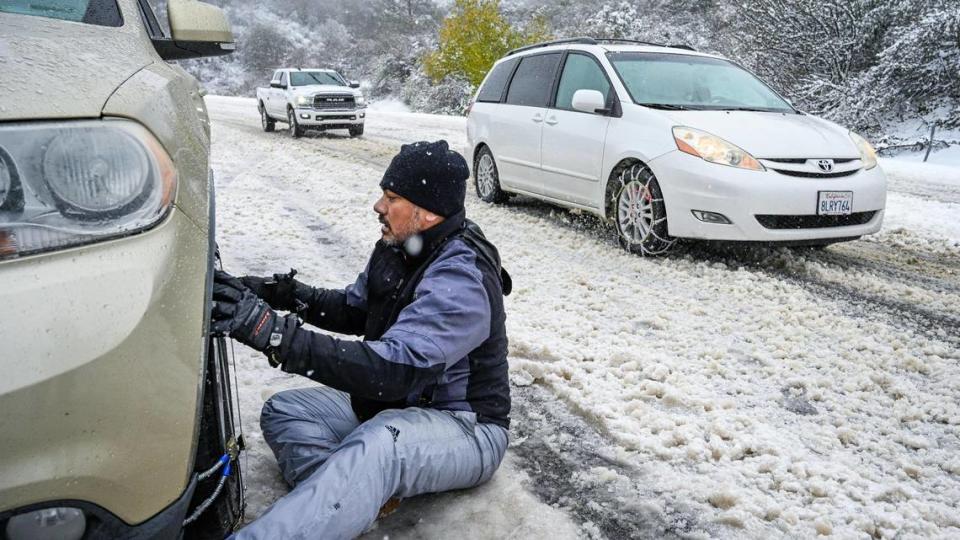 Rodney Tuisavalalo, de Fresno, pone cadenas en su camioneta en la sección de cuatro carriles de la Highway 168 al oeste de Pine Ridge durante una tormenta de nieve, antes de intentar llegar a Shaver Lake para deslizarse en trineo con su familia, el lunes 27 de diciembre de 2021.