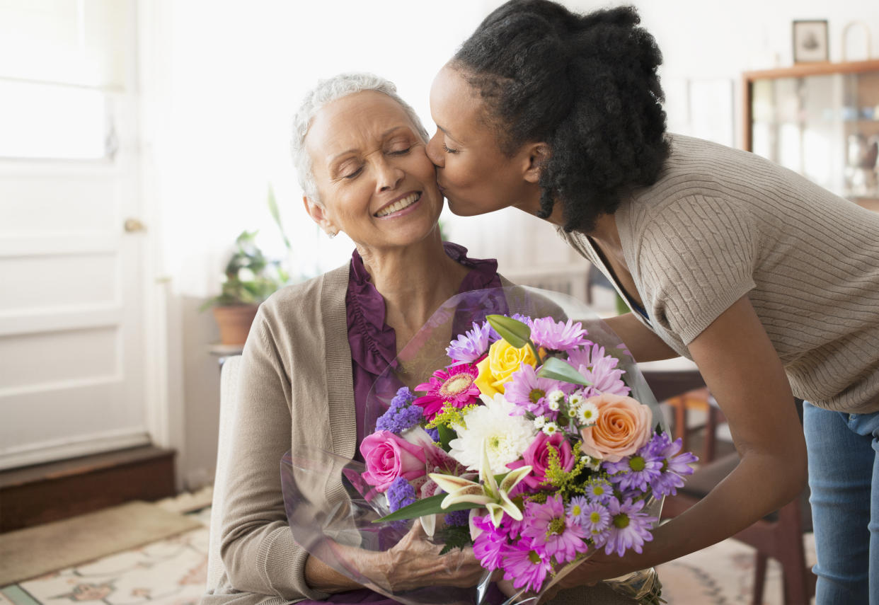 Young Black woman gives older woman a kiss on the cheek while delivering a floral bouquet Mother's Day