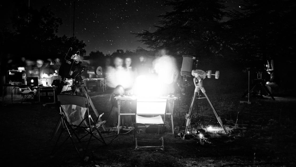  A black and white photograph of a group of people crowded around a telescope. 