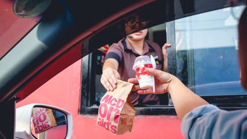 A McDonalds' drive-through worker hands a customer their food out the window