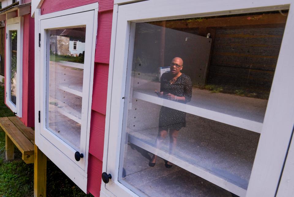 Denise Williams, who started the Inspired Child Project, is reflected in front of her small food pantry and library, which are both empty because she has a hard time getting enough food and books for those in her neighborhood in Montgomery.