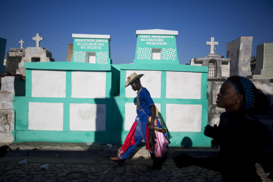 In this Nov. 1, 2018 photo, a voodoo believer walks to Baron Samedi's tomb during the annual Voodoo festival Fete Gede at Cite Soleil Cemetery in Port-au-Prince, Haiti. The most respected along the Fete Gede is Baron Samedi, a lewd representation of life and death, who runs the gate of the Guiné (a kind of Heaven) wearing a black suit and top hat while drinking alcohol, smoking tobacco and following young ladies in a provocative manner. ( AP Photo/Dieu Nalio Chery)