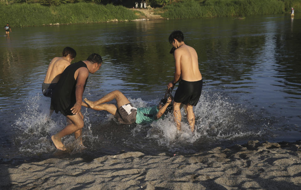 Honduran migrants joke around as they bathe in the Suchiate River, which creates a natural border between Guatemala, below, and Mexico, top, near Tecun Uman, Guatemala, Wednesday, Jan. 22, 2020. The number of migrants stuck at the Guatemala-Mexico border continued to dwindle Wednesday as detentions and resignation ate away at what remained of the latest caravan. (AP Photo/Marco Ugarte)