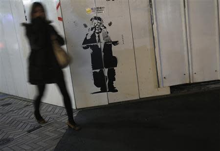 A pedestrian walks past a sticker art made by an artist known as 281 Antinuke, designed in the likeness of Japan's Prime Minister Shinzo Abe, along a street in Tokyo November 26, 2013. REUTERS/Yuya Shino