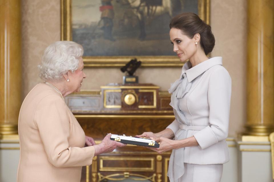 US actress Angelina Jolie (R) is presented with the Insignia of an Honorary Dame Grand Cross of the Most Distinguished Order of St Michael and St George by Britain's Queen Elizabeth II in the 1844 Room at Buckingham Palace in central London, on October 10, 2014. Angelina Jolie was awarded an honorary damehood (DCMG) for services to UK foreign policy and the campaign to end war zone sexual violence. AFP PHOTO/Anthony Devlin/POOL        (Photo credit should read Anthony Devlin/AFP via Getty Images)