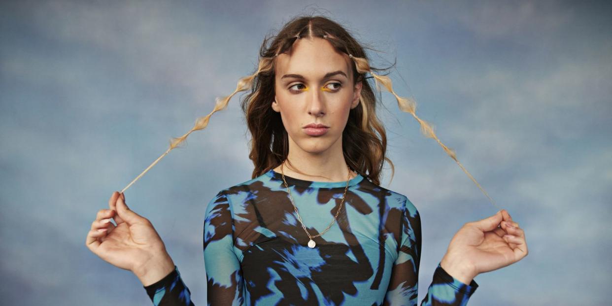 female transgender holding hair against colored background