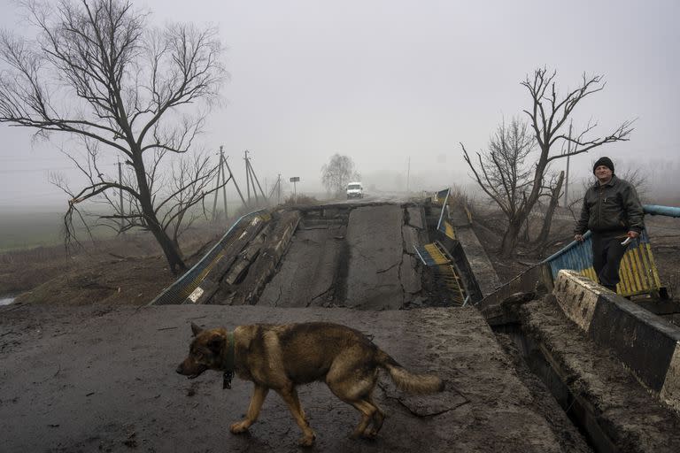 Sasha, de 50 años, espera a su perro Druzhok antes de cruzar un puente destruido por el ejército ruso cuando se retiró de las aldeas en las afueras de Kiev