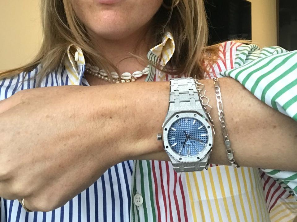 A women holding up an Audemars Piguet watch with her face out frame whilst wearing a multi color striped shirt