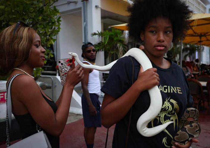Onya Lee-Golightly, 16, right, lets Spring Break tourists take photos with her snakes, Pearl and Osceola, on Sunday, March 19, 2023, on Ocean Drive in Miami. Lee-Golightly and her father are snake breeders.