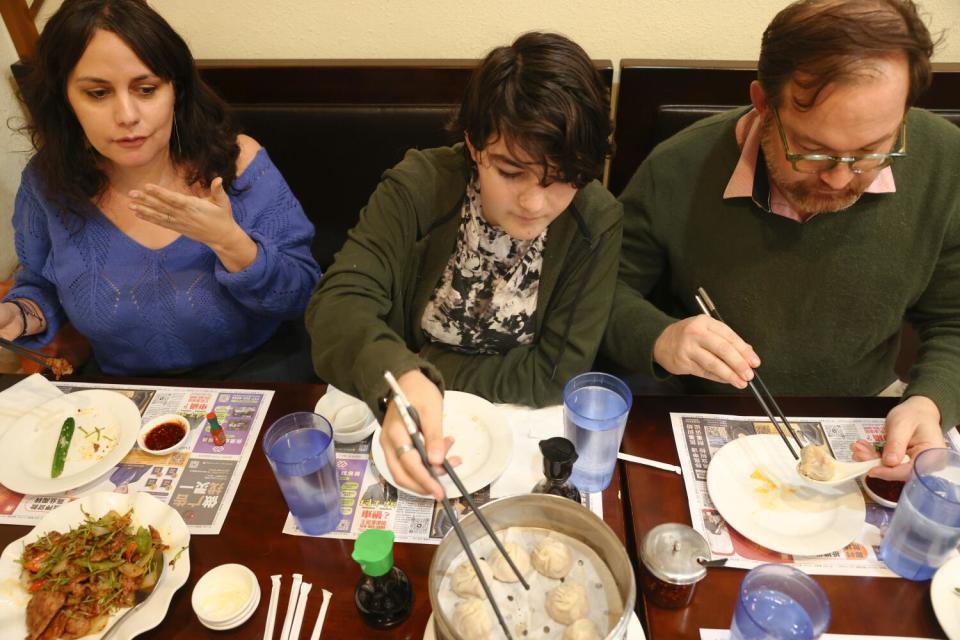 A mother, father and son eat dumplings at a restaurant.