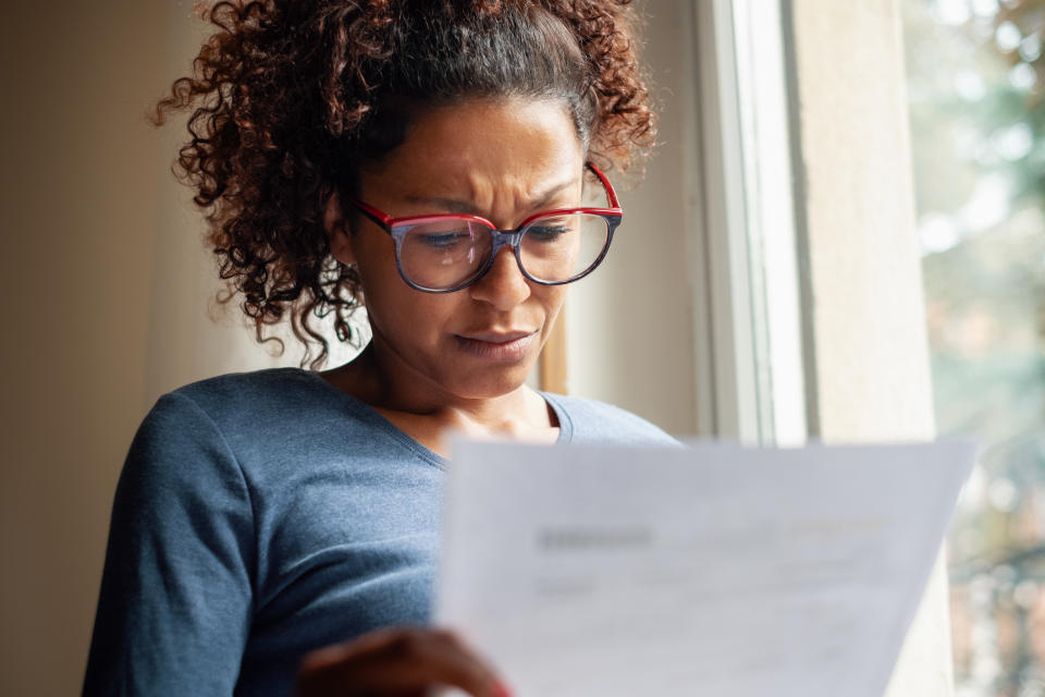 Portrait of woman standing beside window reading rising energy bills (Getty Images)