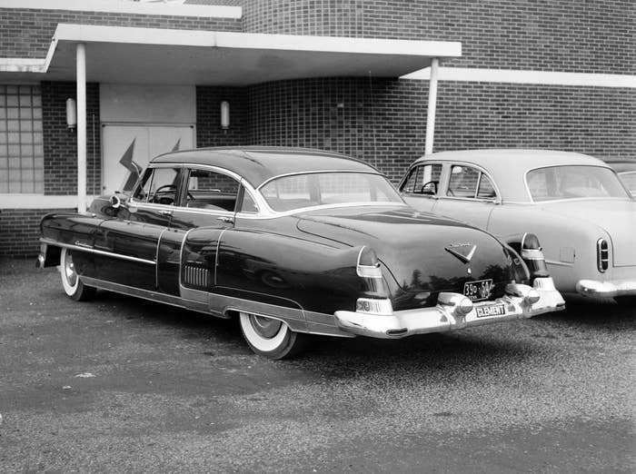 Two classic cars parked outside a brick building with a zigzag pattern on the window