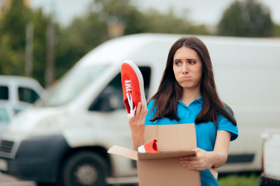 Young woman holds up a shoe above a box, looking disappointed.