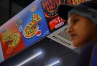 A Domino's staff member stands next to a sign for a 49-rupee pizza at a restaurant in Noida,
