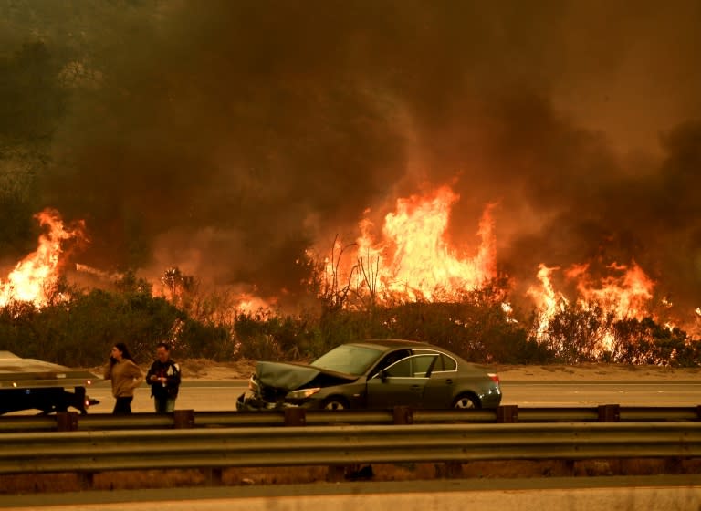 A motorist involved in a traffic accident waits to get towed beside a wall of flames during the Thomas wildfire near Ventura, California