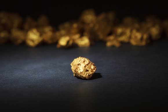 Single gold nugget in foreground, with many gold nuggets in background.