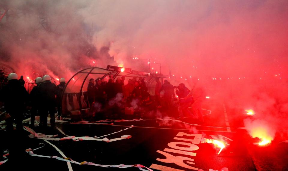 In this Wednesday, April 16, 2014 photo PAOK's fans throw flares onto Olympiakos' bench before a semi-final of the Greek Cup in the northern port city of Thessaloniki. Police in Thessaloniki have arrested a PAOK fan accused of dumping a crate of fish on the visiting Olympiakos bench, in a jibe that delayed a tense Greek cup semi-final for more than an hour. Another six PAOK supporters were arrested during clashes with police before and after Thursday’s match, which PAOK won 1-0 to advance on aggregate. The game was repeatedly halted by on-turf brawls, resulting in three red cards, while PAOK fans in the stands lit thousands of flares, and several were thrown on the pitch. (AP Photo/InTime Sports, Yorgos Matthaios) GREECE OUT