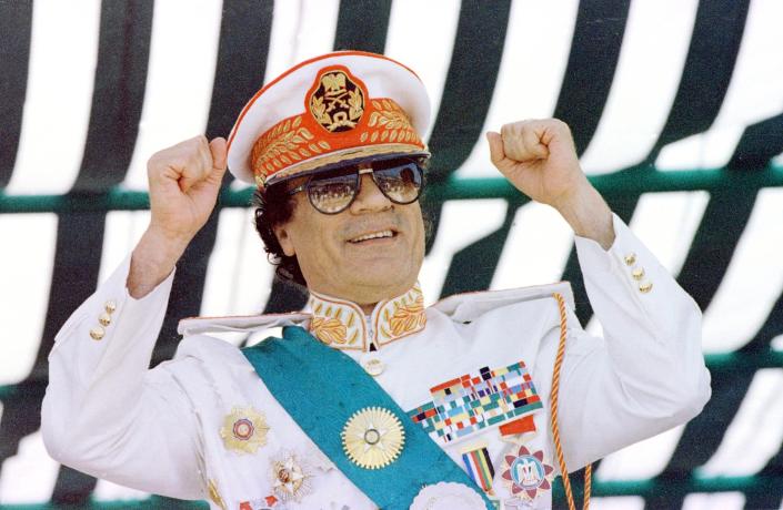 Moammar Gadhafi stands with fists raised at a military parade. 