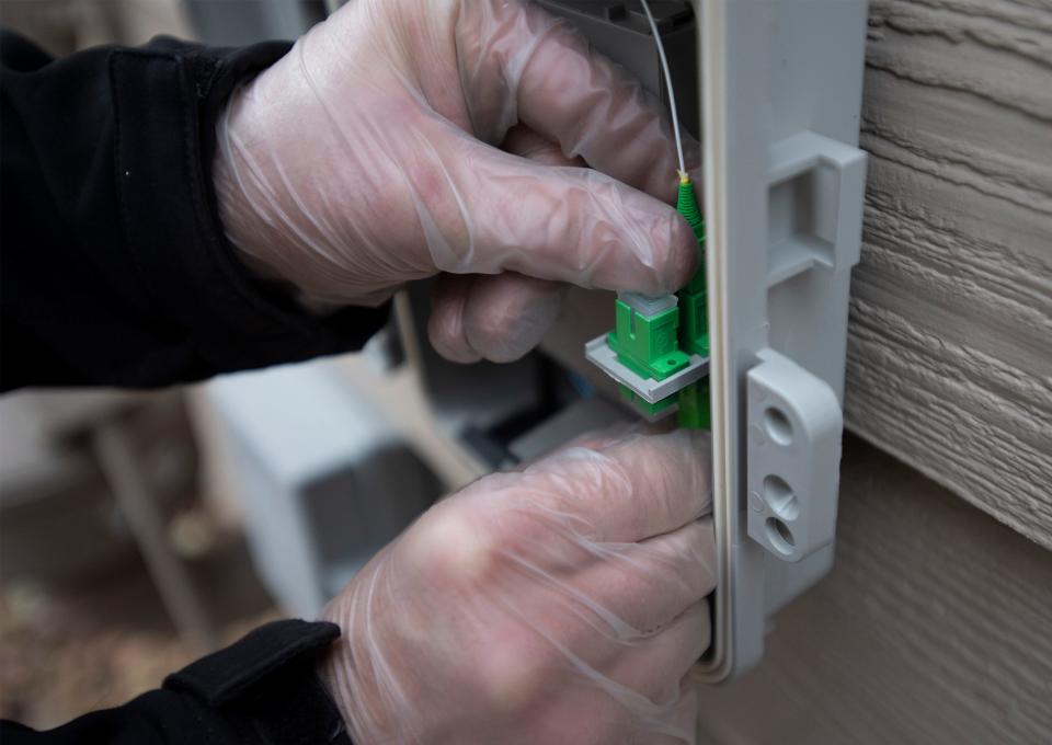 Marcus Baker, a technician with OnTrac, connects a fiber optic cable attachment to a mounted network interface device during an installation for a Connexion customer in Fort Collins, Colo. on Thursday, Jan. 21, 2021.