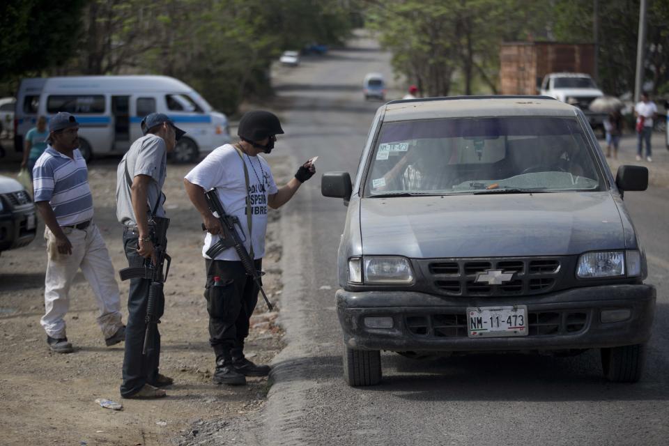 Armed men belonging to the Self-Defense Council of Michoacan (CAM) check the documents of people in a vehicle at a checkpoint set up by the vigilante group in La Mira on the outskirts of the seaport of Lazaro Cardenas in western Mexico, Friday, May 9, 2014. A ceremony on Saturday will mark the registering of thousands of guns by the federal government and an agreement that the self-defense groups will either join a new official rural police force or return to their normal lives and act as voluntary reserves when called on. But tension remained on Friday in the coastal part of the state outside the port of Lazaro Cardenas, where some self-defense groups plan to continue as they are, defending their territory without registering their arms. (AP Photo/Eduardo Verdugo)