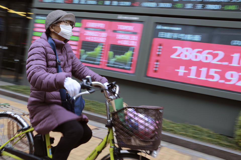 A woman cycles past by an electronic stock board of a securities firm in Tokyo, Wednesday, Jan. 27, 2021. Stocks were mixed in Asia on Wednesday after a lackluster session on Wall Street. (AP Photo/Koji Sasahara)