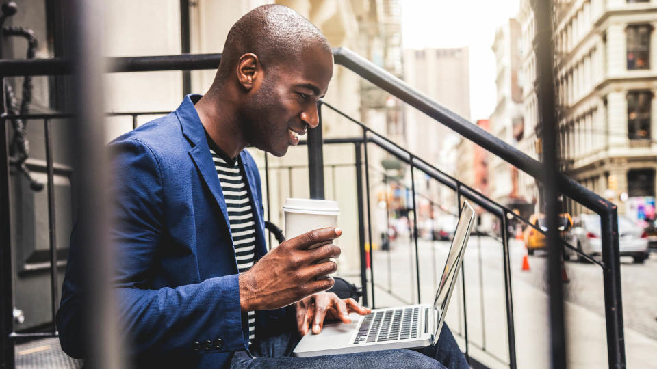 Man texting on laptop seated on steps on the streets in Soho New York.