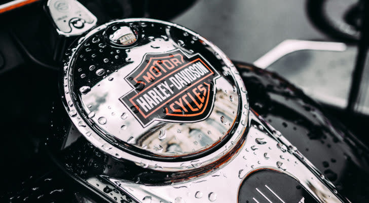 A close-up photograph of the tank to a Harley-Davidson motorcycle with raindrops on it.