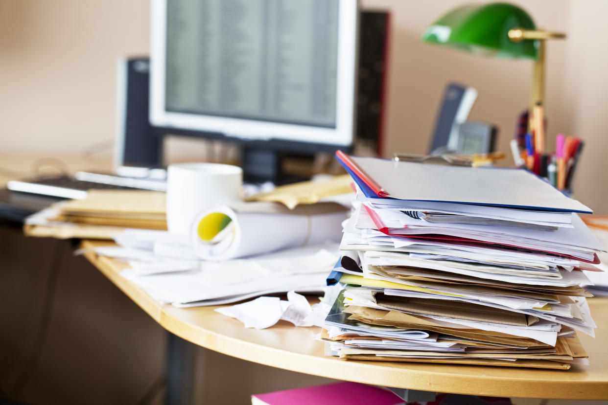 A pile of papers stacked on a cluttered office desk.