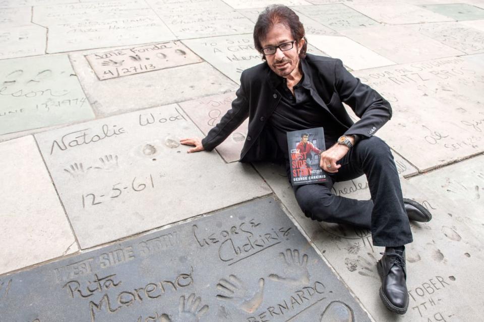 <div class="inline-image__caption"><p>George Chakiris poses with his book next to his handprints during the ceremony unveiling the new plaque honoring all the 100+ Oscar winners who got their handprint-footprints at the TCL Chinese Theater, April 21, 2021, in Hollywood, California.</p></div> <div class="inline-image__credit">Valerie Macon/AFP/Getty</div>