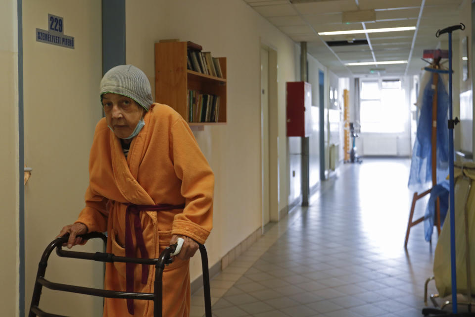 An elderly homeless woman walks in the corridor of the hospital for the homeless in Budapest, Hungary, Wednesday, April 14, 2021. A bitter conflict has emerged between Hungary’s right-wing government and the liberal leadership of the country's capital city over a hospital for the homeless that may soon have to close. The Budapest hospital provides medical and social services and shelter to more than 1,000 people annually. But the Hungarian government has ordered it to vacate the state-owned building it occupies. Budapest's mayor says the eviction will risk the lives of the hospital's homeless patients as Hungary struggles with a deadly COVID-19 surge. (AP Photo/Laszlo Balogh)