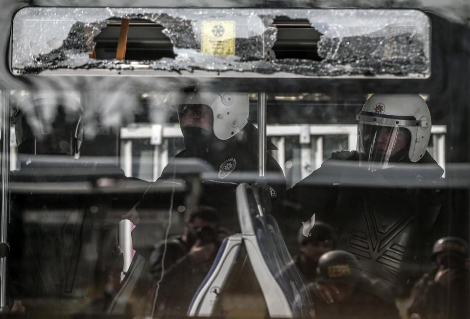 Riot police officers wait in a damaged bus as thousands of people march for Berkin Elvan, a Turkish teenager who was in a coma since being hit on the head by a tear gas canister fired by police during anti-government protests in the summer of 2013, during his funeral in Istanbul, Turkey, Wednesday, March 12, 2014. On Wednesday, thousands converged in front of a house of worship calling for Prime Minister Recep Tayyip Erdogan to resign. (AP Photo/Emrah Gurel)