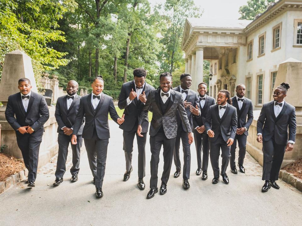 A groom and his groomsmen walk together wearing tuxedos.