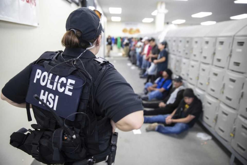 This image released by the US Immigration and Customs Enforcement (ICE) shows a Homeland Security Investigations (HSI) officer guarding suspected illegal aliens on August 7, 2019. Officers detained approximately 680 aliens who were unlawfully working at at seven agricultural processing plants across Mississippi. - US officials said that some 680 undocumented migrants were detained in a major series of raids on August 7, at food processing plants in the southeastern state of Mississippi, part of President Donald Trump's announced crackdown on illegal immigration. "Special agents executed administrative and criminal search warrants resulting in the detention of approximately 680 illegal aliens," said Mike Hurst, US Attorney for the Southern District of Mississippi. (Photo by HO / US Immigration and Customs Enforcement / AFP)