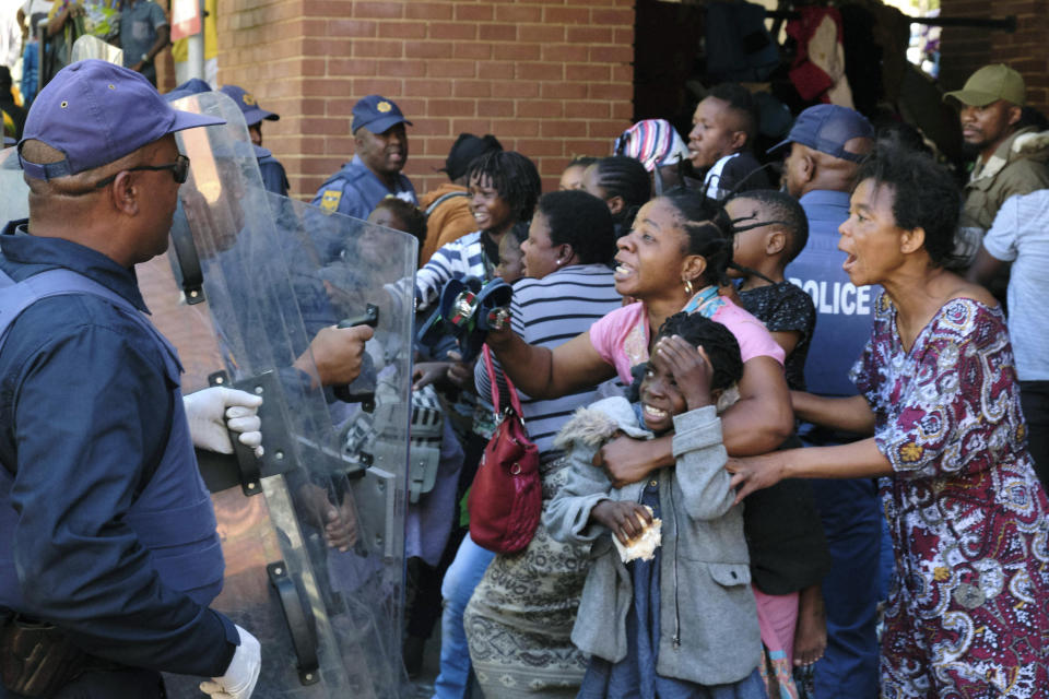 Refugees, mostly from the Democratic Republic of Congo, face off with South African Police officers, at the United Nations High Commissioner for Refugees (UNHCR) compound in Pretoria, South Africa, Friday, Nov. 15, 2019. Police removed about 150 refugees who the United Nations refugee agency says forced their way into its compound while protesting recent anti-immigrant attacks. (AP Photo/Elna Schütz)