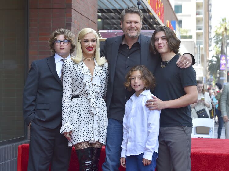 Gwen Stefani in a white dress and Blake Shelton in formal wear pose with three young men at the Hollywood Walk of Fame