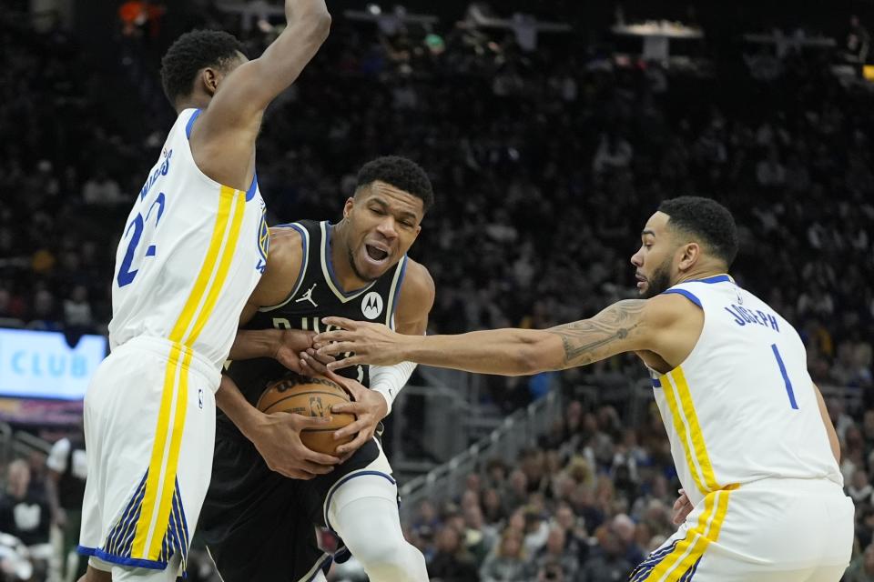 Milwaukee Bucks' Giannis Antetokounmpo is fouled as he drives between Golden State Warriors' Andrew Wiggins and Cory Joseph during the first half of an NBA basketball game Saturday, Jan. 13, 2024, in Milwaukee. (AP Photo/Morry Gash)