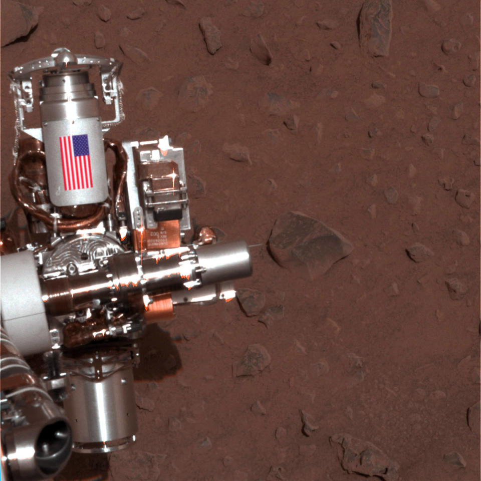 This image provided by NASA shows the piece of metal with the American flag on it is made of aluminum recovered from the site of the World Trade Center towers in New York City on Mars Rover Spirit that serves as a cable guard for Spirit’s rock abrasion tool as well as a memorial to the victims of the Sept. 11, 2001, terrorist attacks. Mars Rover Opportunity has an identical piece. Ten years after NASA landed two rovers on Mars on a 90-day mission, one rover is still exploring, and the project has generated hundreds of thousands of images from the Martian surface. Now the Smithsonian’s National Air and Space Museum is presenting more than 50 of the best photographs from the two Mars rovers in an art exhibit curated by the scientists who have led the ongoing mission. (AP Photo/NASA/JPL-Caltech/Cornell University)