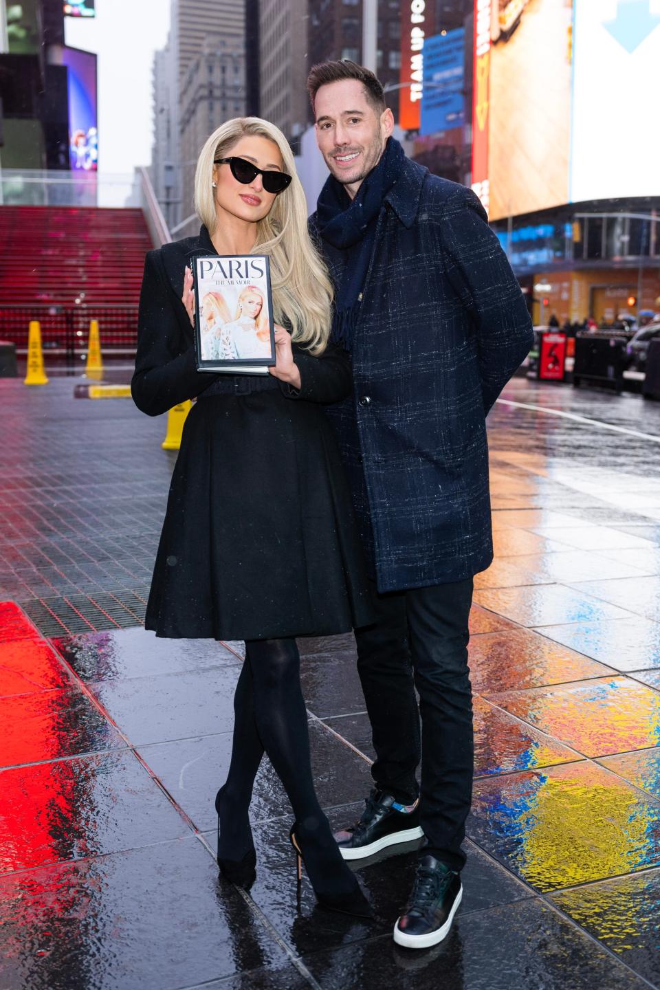 Paris Hilton holding her new memoir next to her husband Carter Reum in Times Square in New York City.