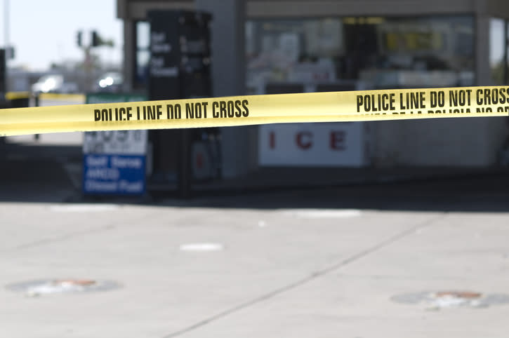 Police tape with "Police Line Do Not Cross" blocks the view of a storefront and surrounding area, indicating a restricted crime scene