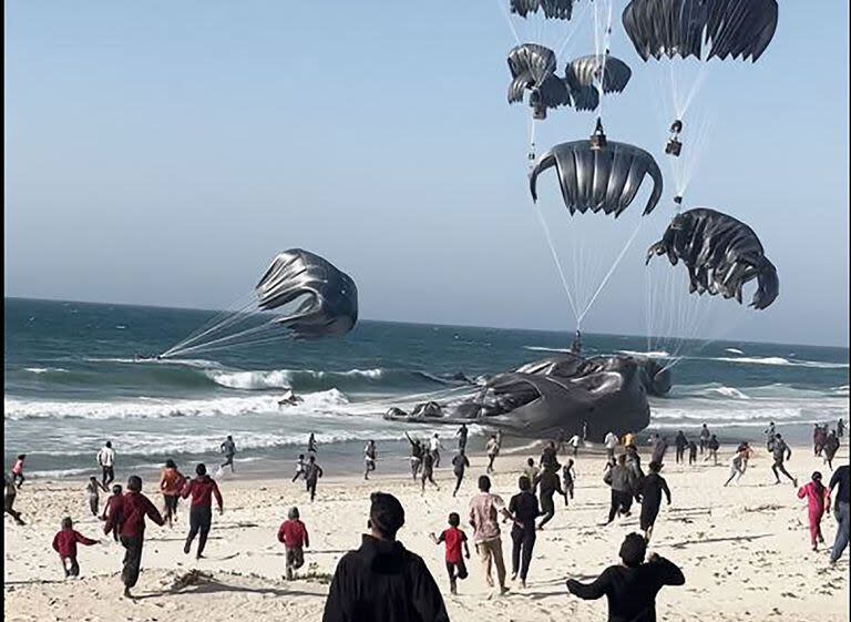 Palestinos corriendo hacia los paquetes con ayuda humanitaria lanzados desde aviones hacia la Franja de Gaza, el 2 de marzo de 2024 (Aline MANOUKIAN / AFP)