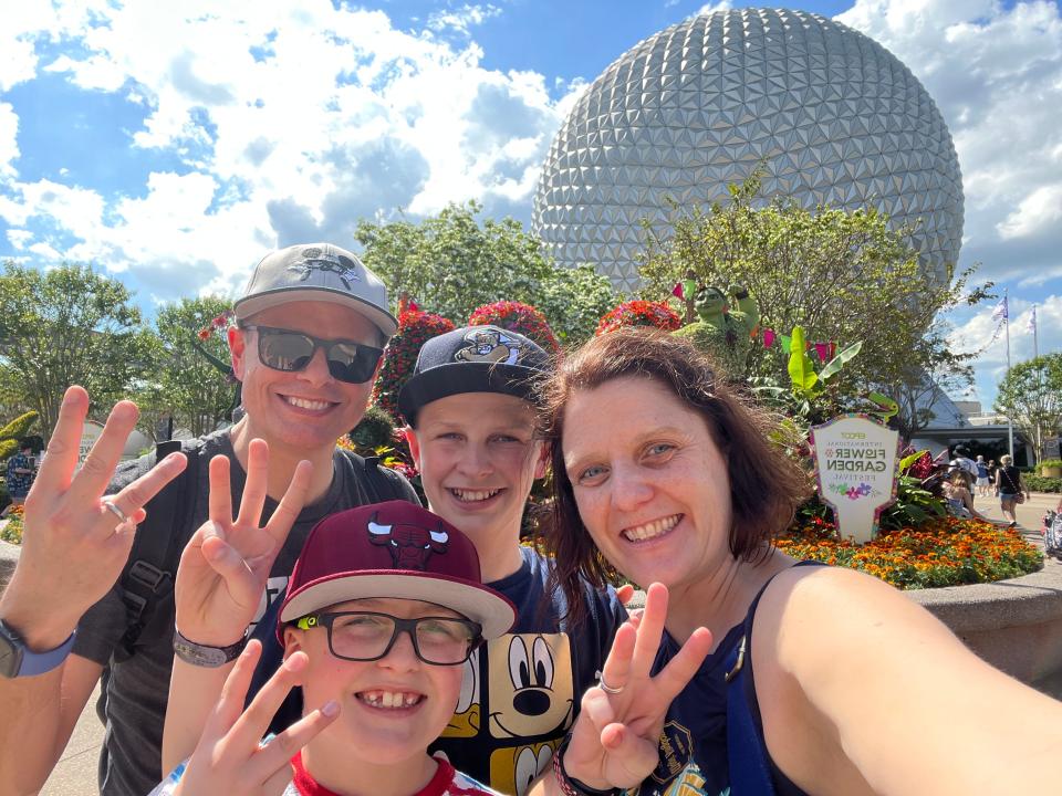 kari and her family holding up three fingers in front of the epcot ball at disney world