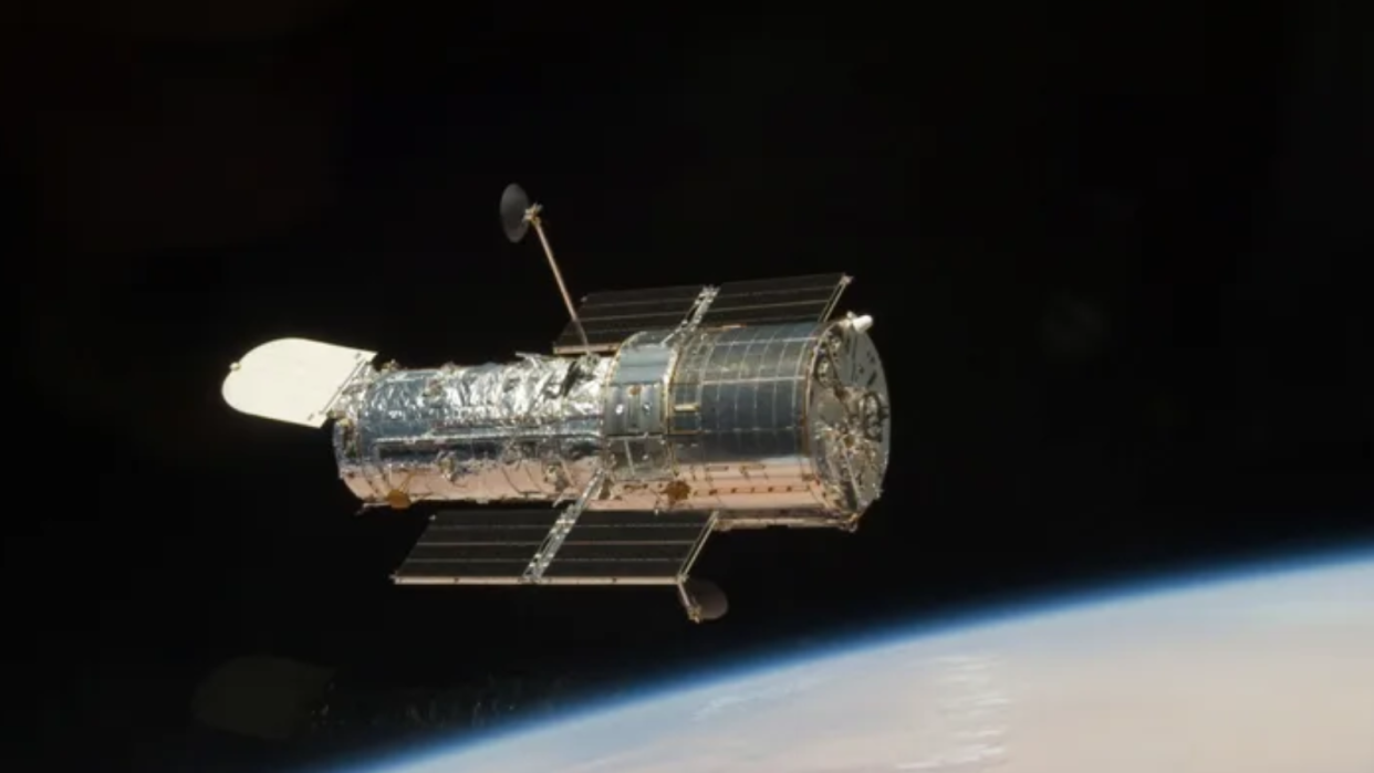  Closeup of a silver telescope in space, with earth in the background. 